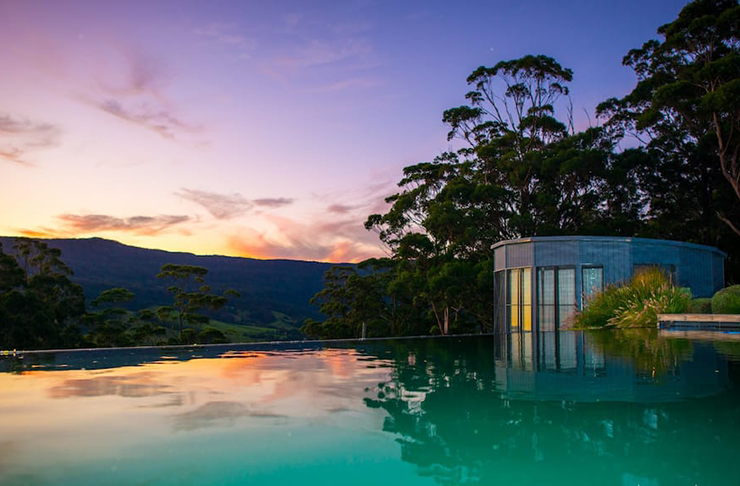 An infinity pool over looking a lush green hillside in the evening sun.