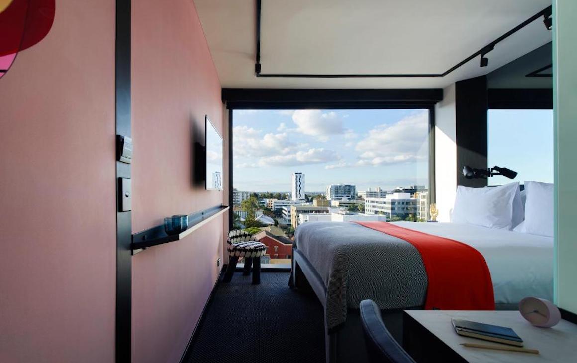 a contemporary hotel room with pink-hued walls and large window