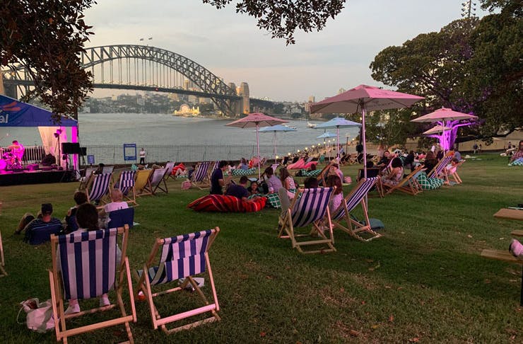 Deck chairs set up on the green lawn of the Royal Botanic Garden in Sydney, with views over the harbour and Sydney Harbour Bridge. 