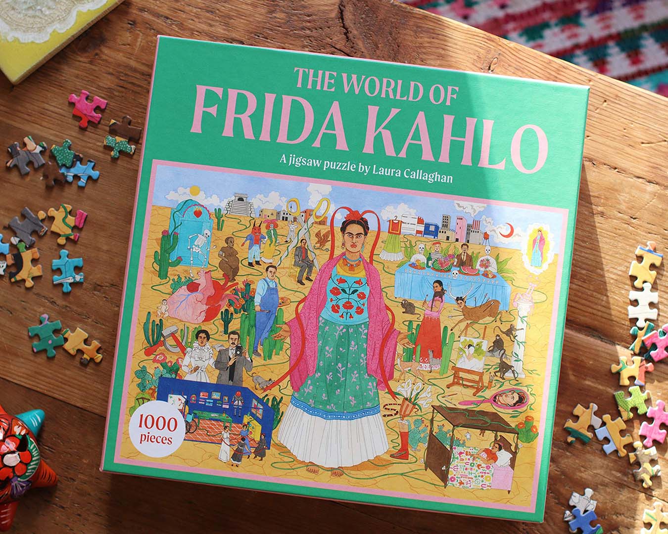 A puzzle box, featuring an illustration of Frida Kahlo, sits on wooden table with a few pieces scattered around.