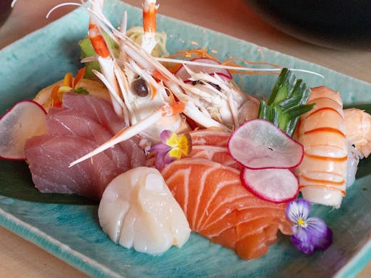 A plate of various sashimi and decorative flowers.