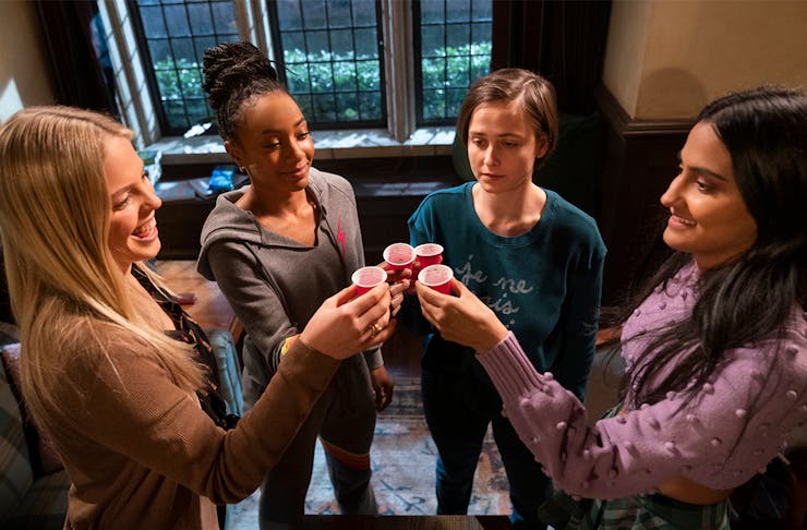 four teenage girls hold up a shot glass in a cheers. 