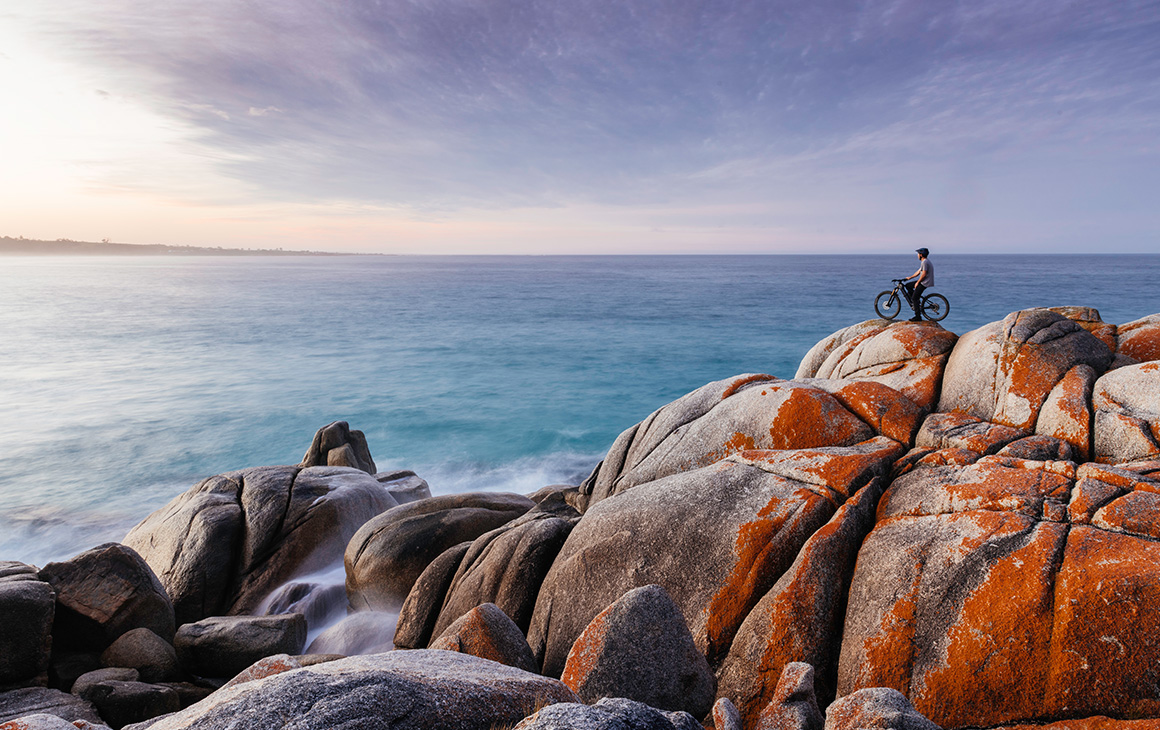 a person on a bike sits on the edge of the bay of fires