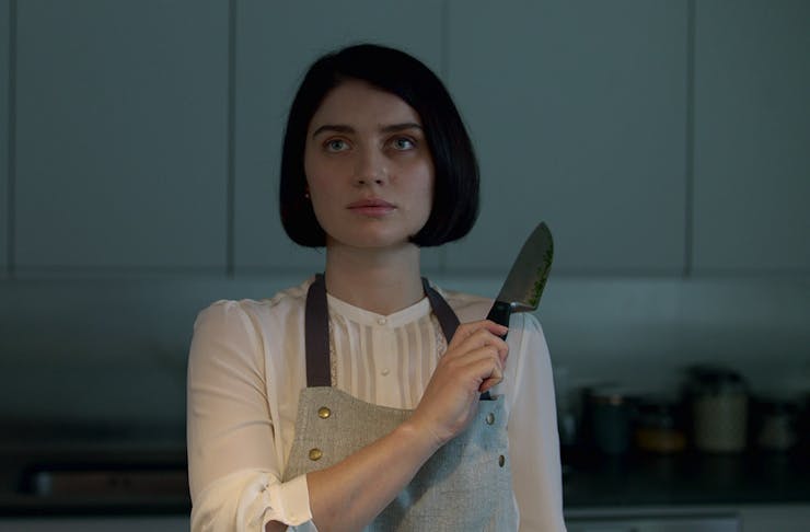 a woman holds up a knife, while standing in the kitchen.