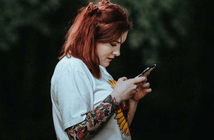 person with shoulder length hair and tattoos playing on smartphone