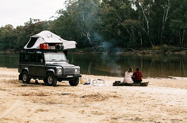 two people sitting on log on sandbank next to a 4wd with a tent on top