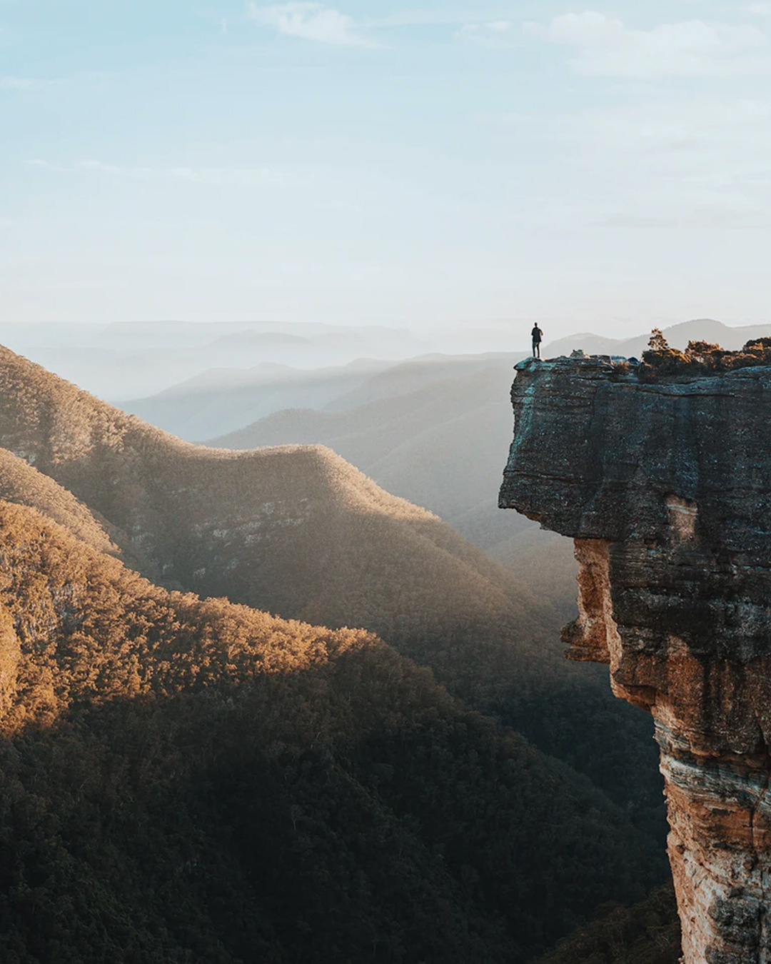 view from mountain in sydney's blue mountain ranges, man standing on edge of cliff