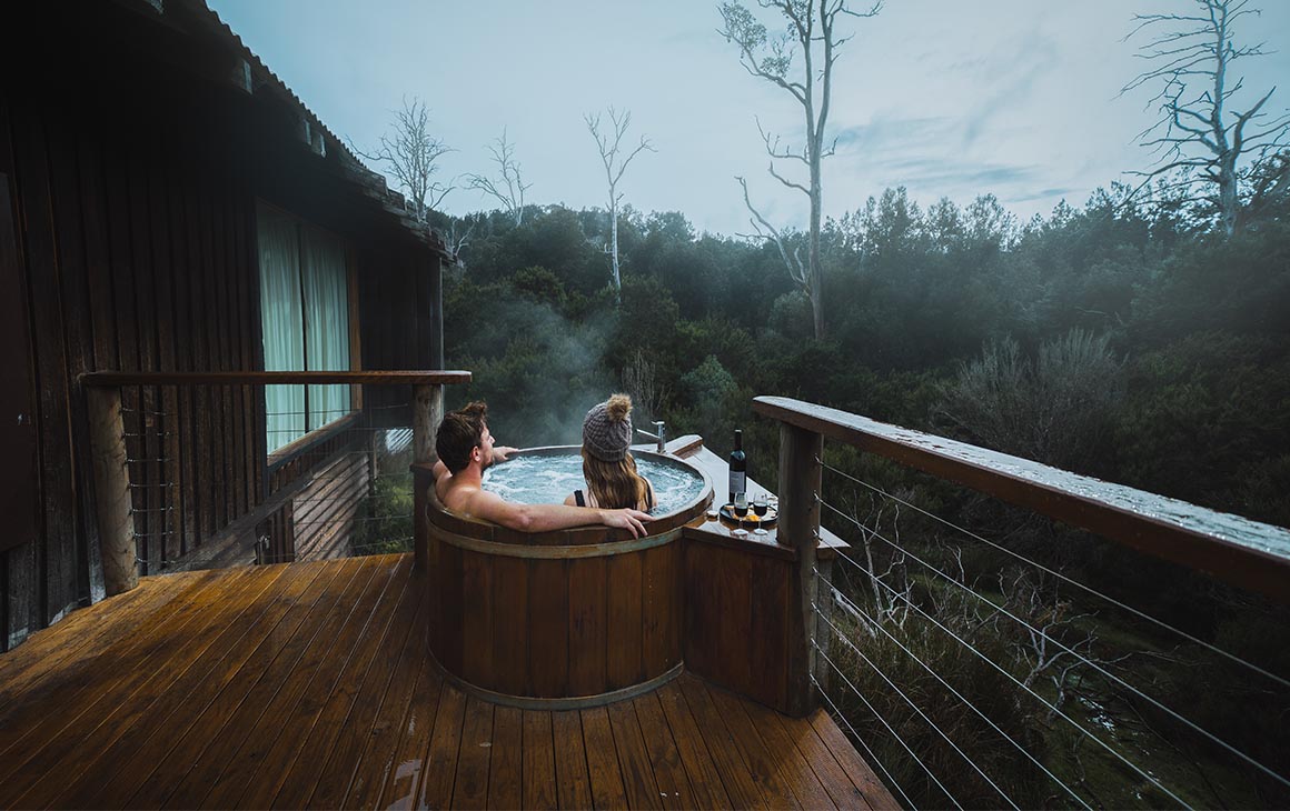 A couple soak in a free-standing wooden tub on a balcony 