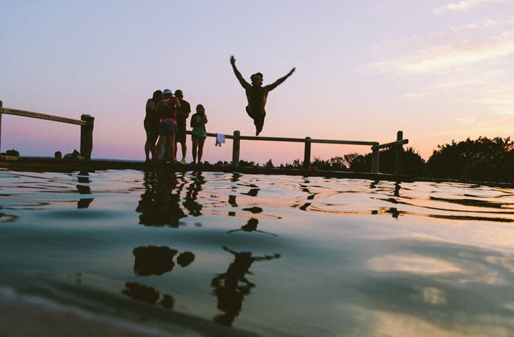 people jumping into ocean pool at sunset