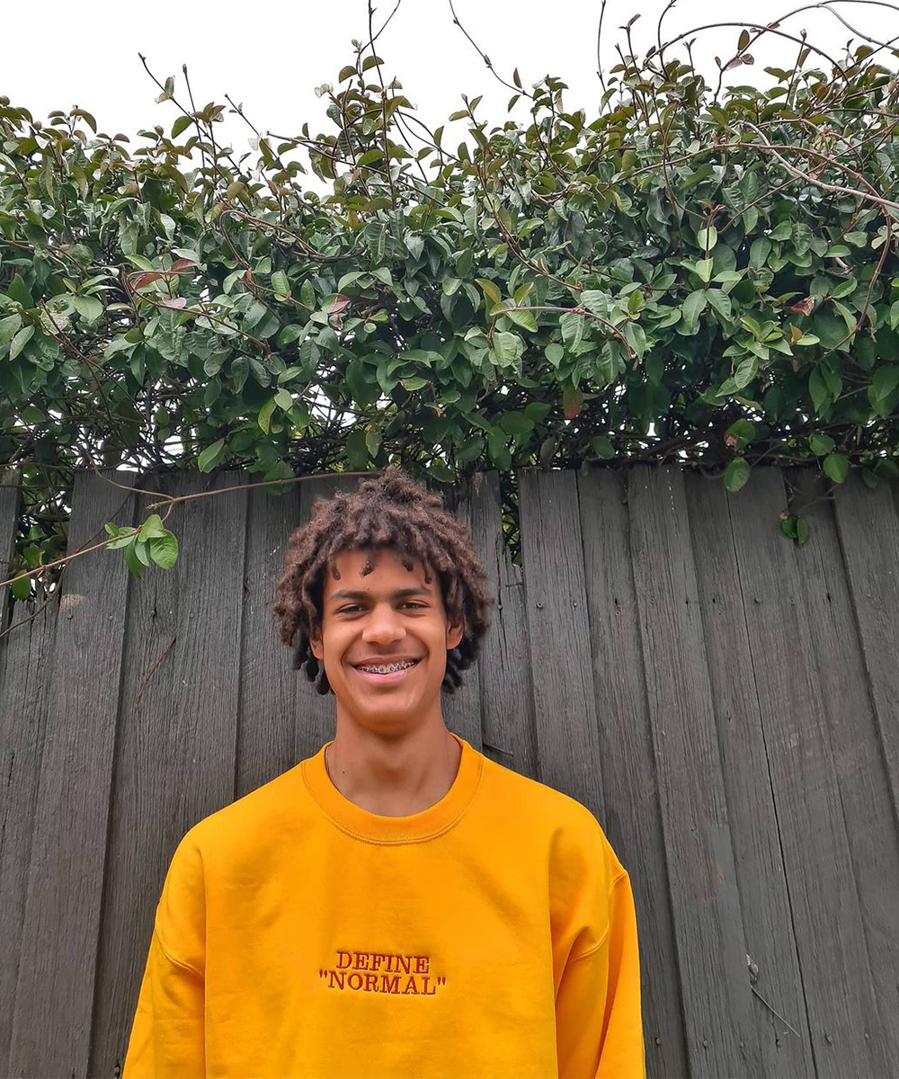 a young man wears a bright yellow jumper with the text 'define normal' on it.