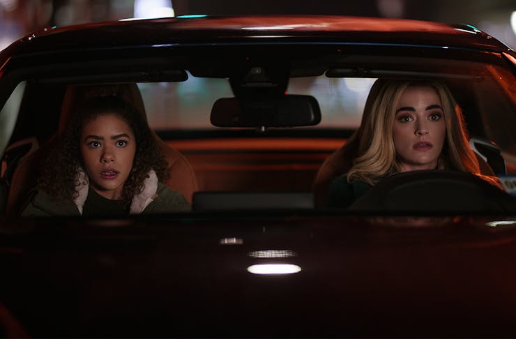 two young women sit behind the wheel of a parked car at night