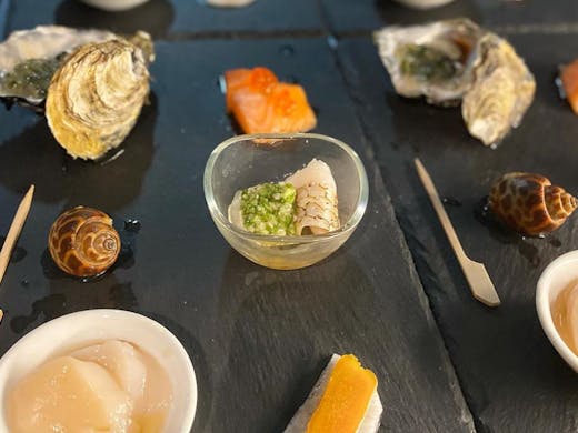 A collection of small Japanese dishes including oysters and snails all lined up. 