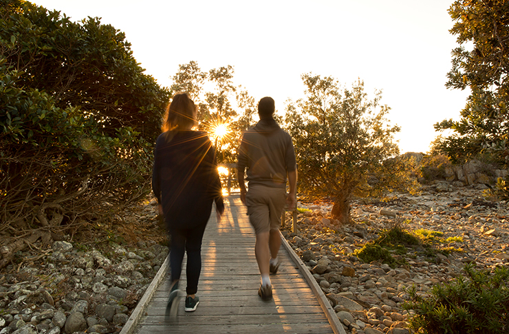 two people walking along boardwalk into sunrise