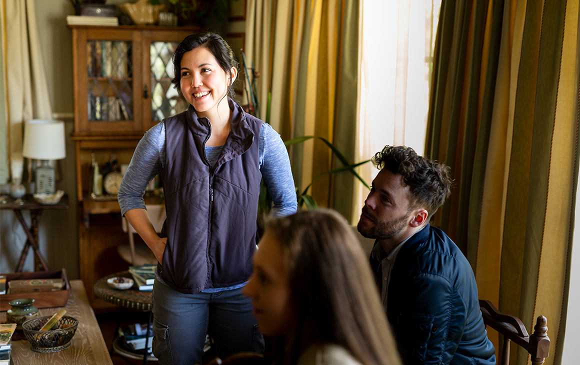 Director Natalie Erika James on set smiles while directing a man and a woman in a lounge room.
