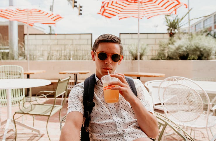 a young man wearing a backpack sips from a drink.
